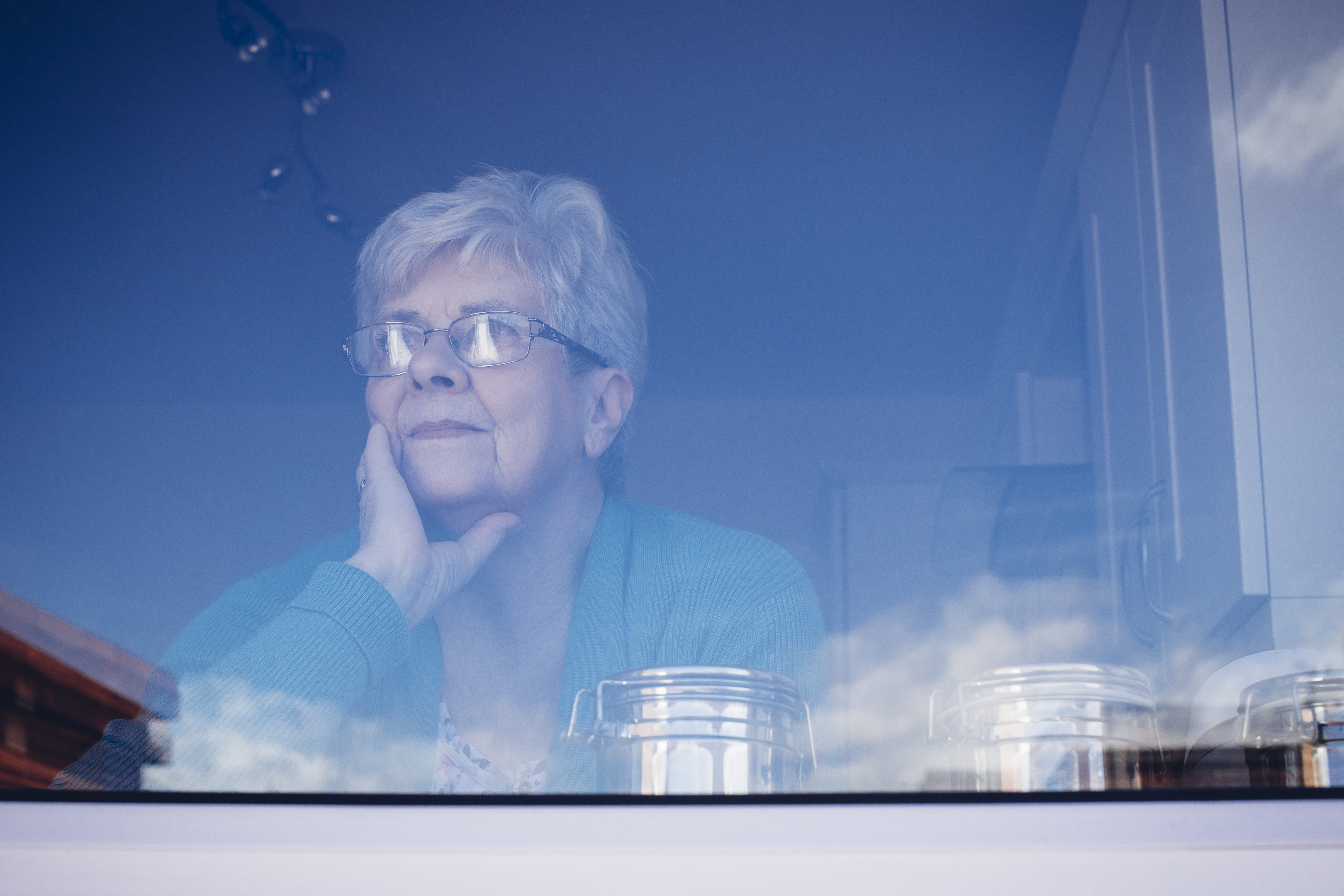 older woman with glasses seen through a window