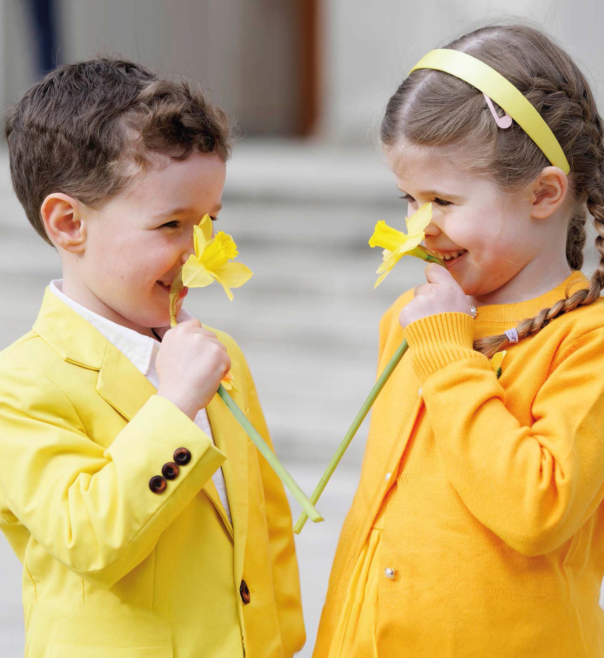 Kids in yellow clothes smiling and smelling with yellow daffodils.