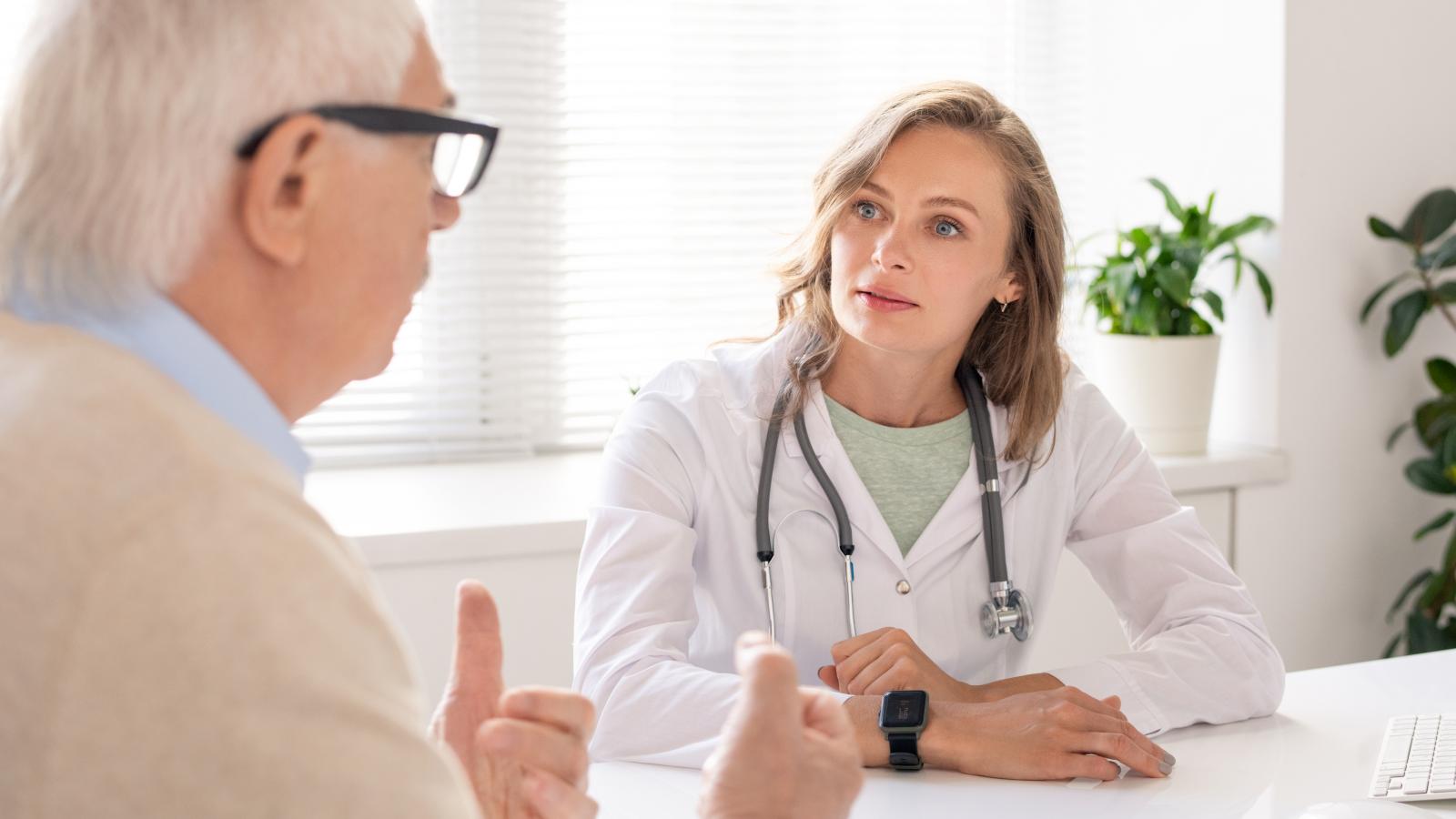 An elderly man wearing glasses explains something to a young female doctor.